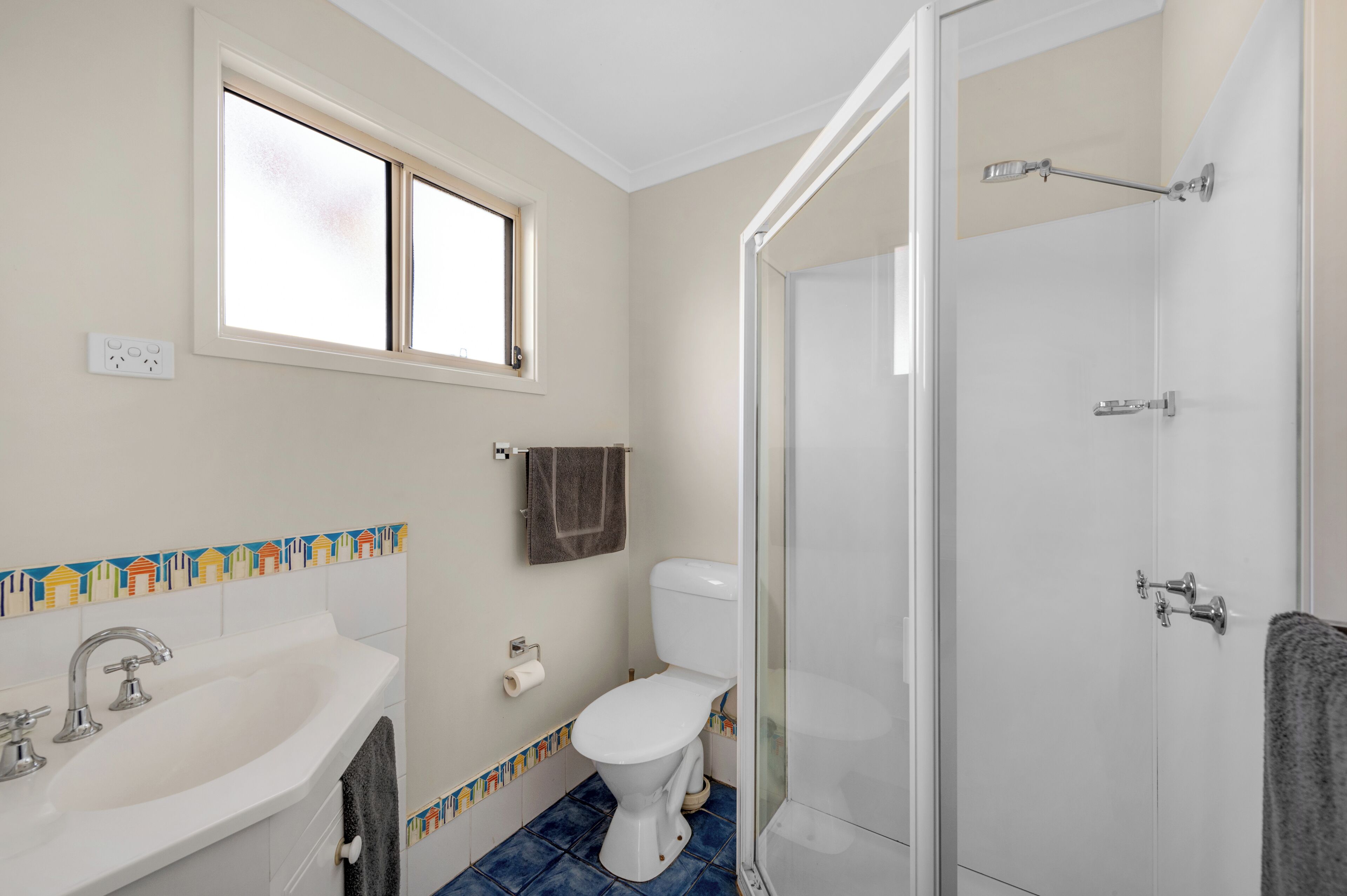Ein Badezimmer mit einem weißen Waschbecken, einer Toilette und einer Dusche. Über dem Waschbecken befindet sich ein Fenster und eine Handtuch an der Wand.