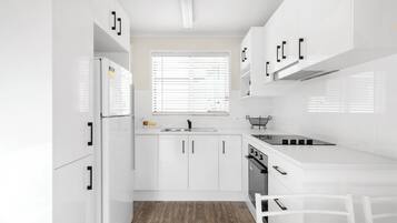 Una cocina moderna con armarios blancos, horno empotrado y ventana con persianas.