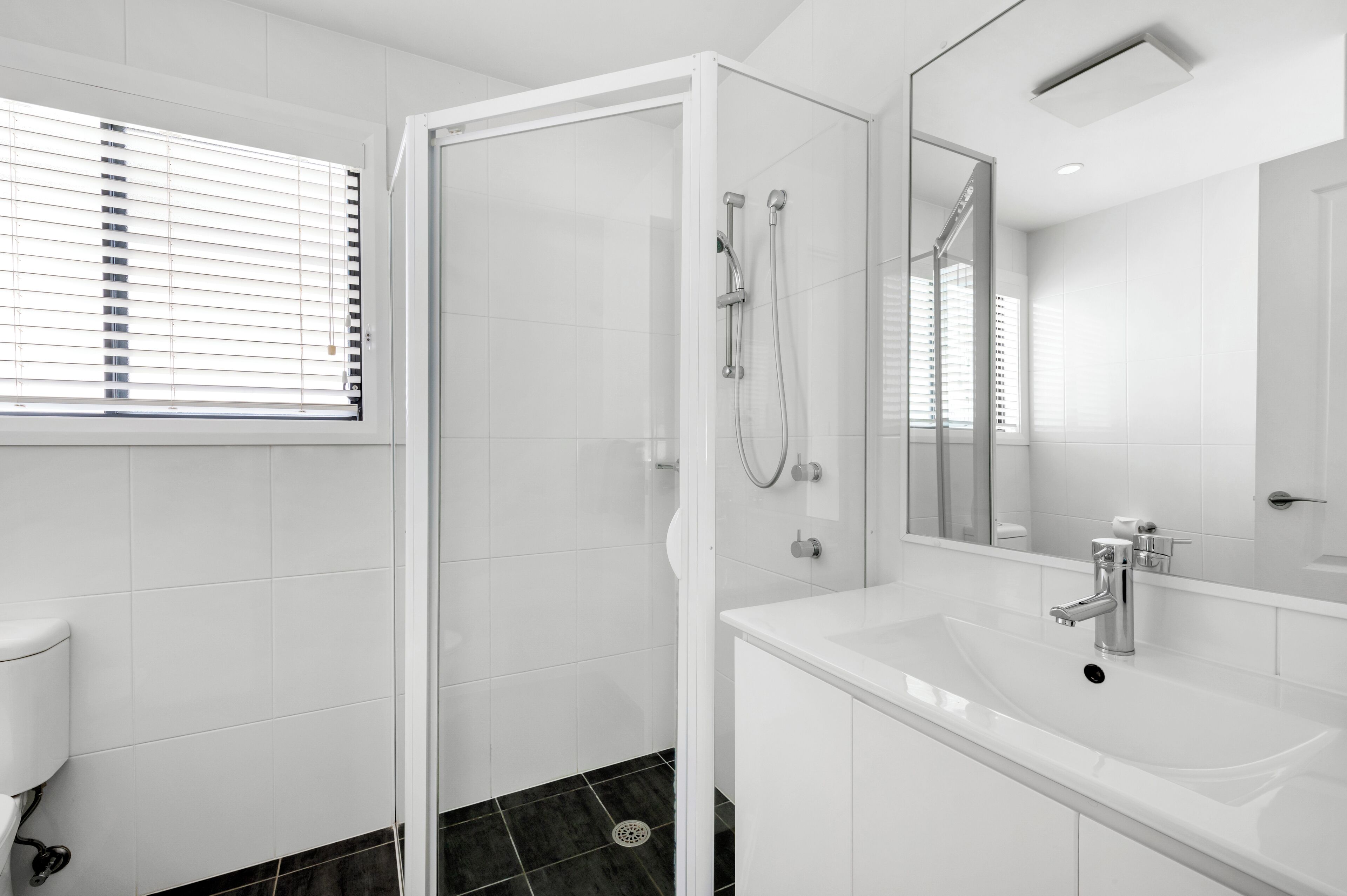 Un baño moderno con cabina de ducha de vidrio, un lavamanos blanco y un espejo grande.