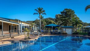 A swimming pool with lounge chairs, a covered seating area, and a building with a covered patio. - Mountain View Resort (Shoalhaven Heads)