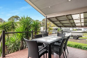 A covered outdoor patio with a table and chairs, surrounded by greenery and a truck in the background. - Mountain View Resort (Shoalhaven Heads)