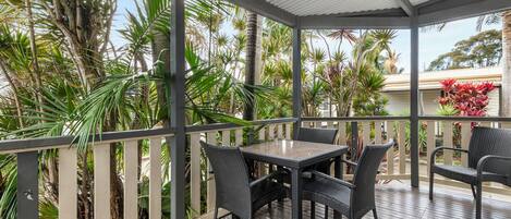 A covered outdoor area with a wooden deck, wicker furniture, and tropical plants.
