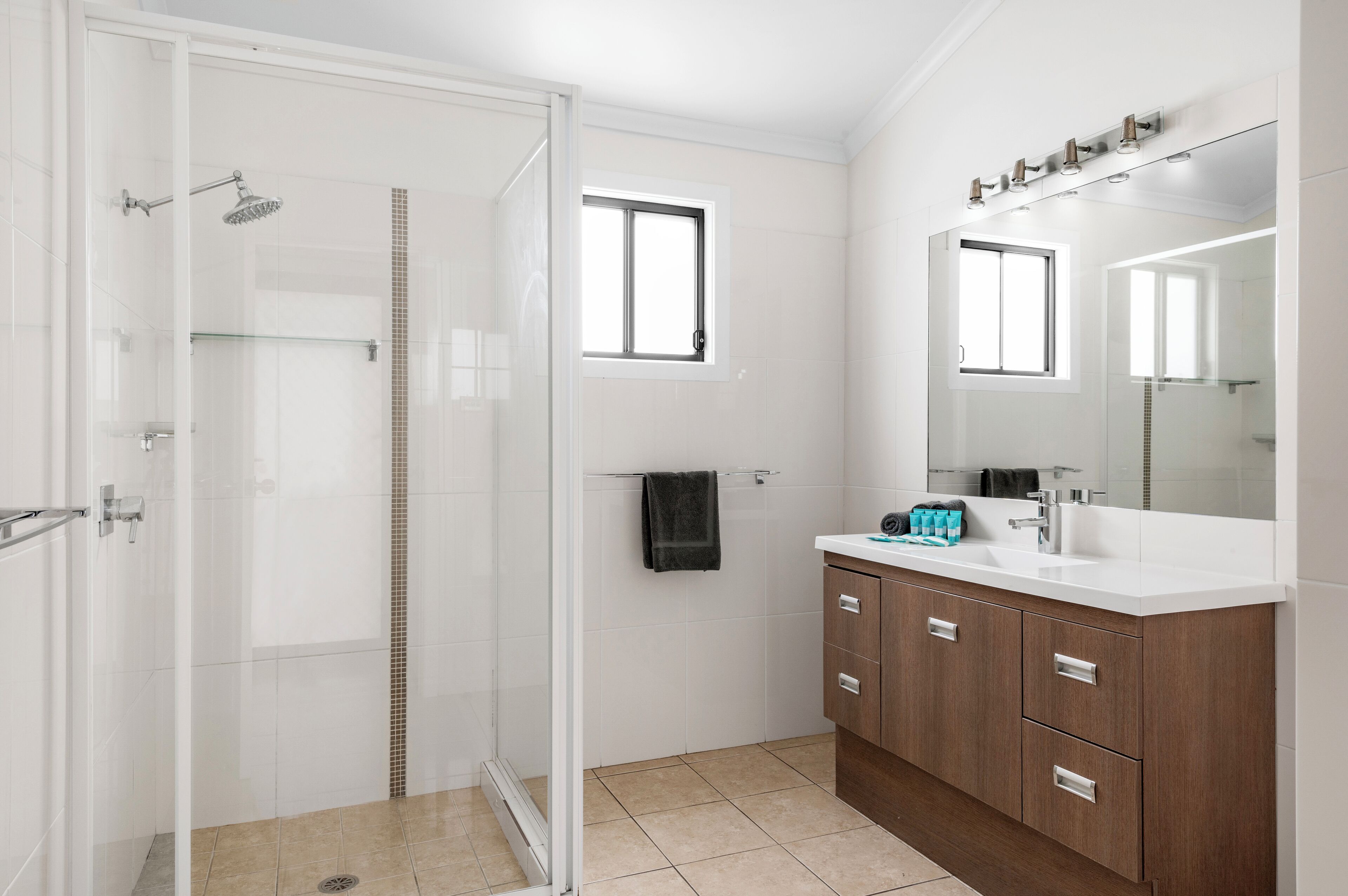 A modern bathroom with a glass-enclosed shower, a large mirror, and wooden cabinets.