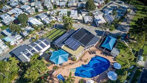 An aerial view of a residential area with multiple houses, a swimming pool, and solar panels on the roofs. - Mountain View Resort (Shoalhaven Heads)