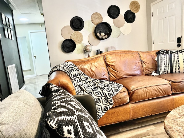Un canapé en cuir marron agrémenté de coussins à motifs, une table basse ronde et un mur décoré d’objets circulaires et ronds.