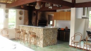 A rustic kitchen with a stone island, wooden chairs, and a brick oven.
