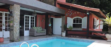 A swimming pool with a stone pillar and a wicker sofa.