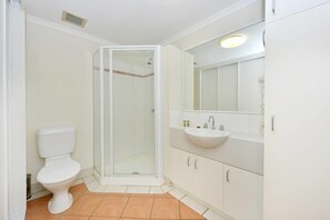 Une salle de bain comprenant des toilettes, un espace douche, un lavabo et des meubles de rangement.