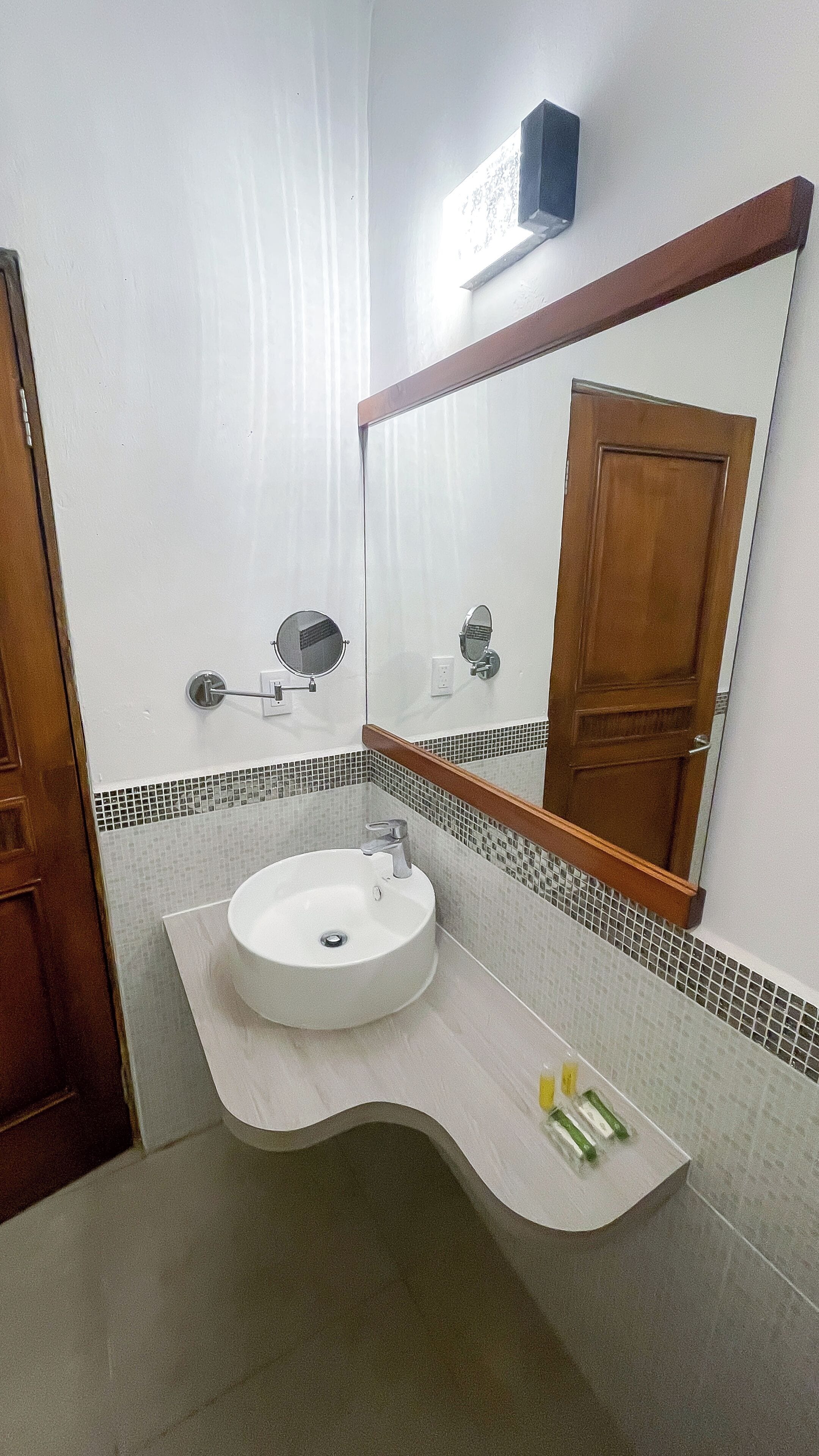 Un baño con un lavamanos blanco, un espejo y una puerta de madera.