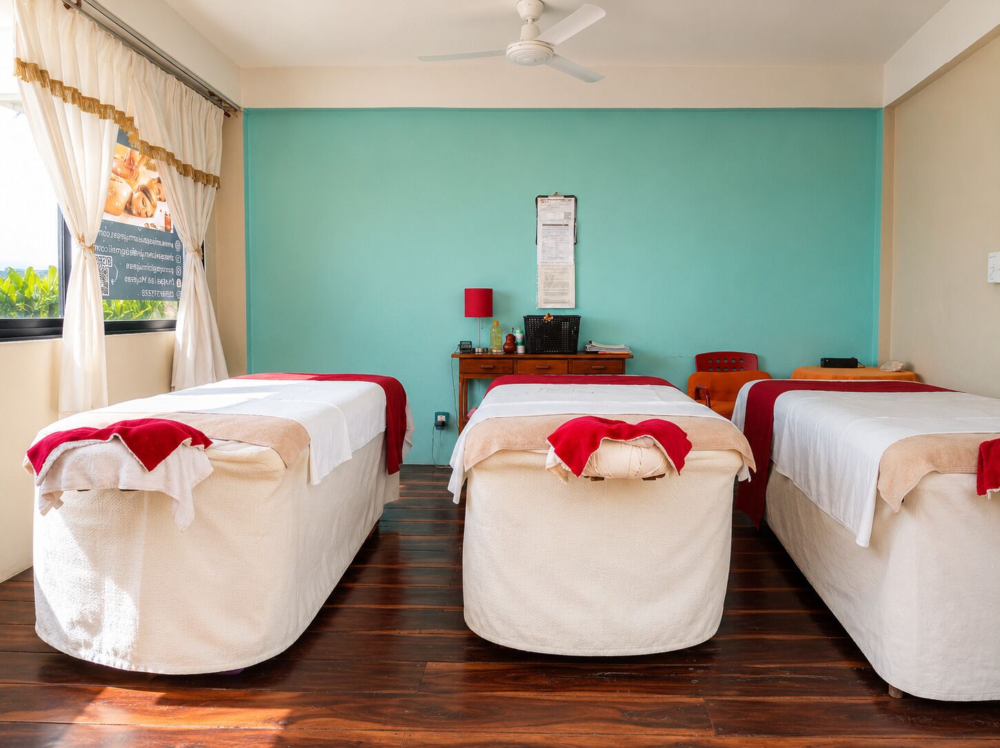 A room with three beds, a desk with a lamp, and a ceiling fan.