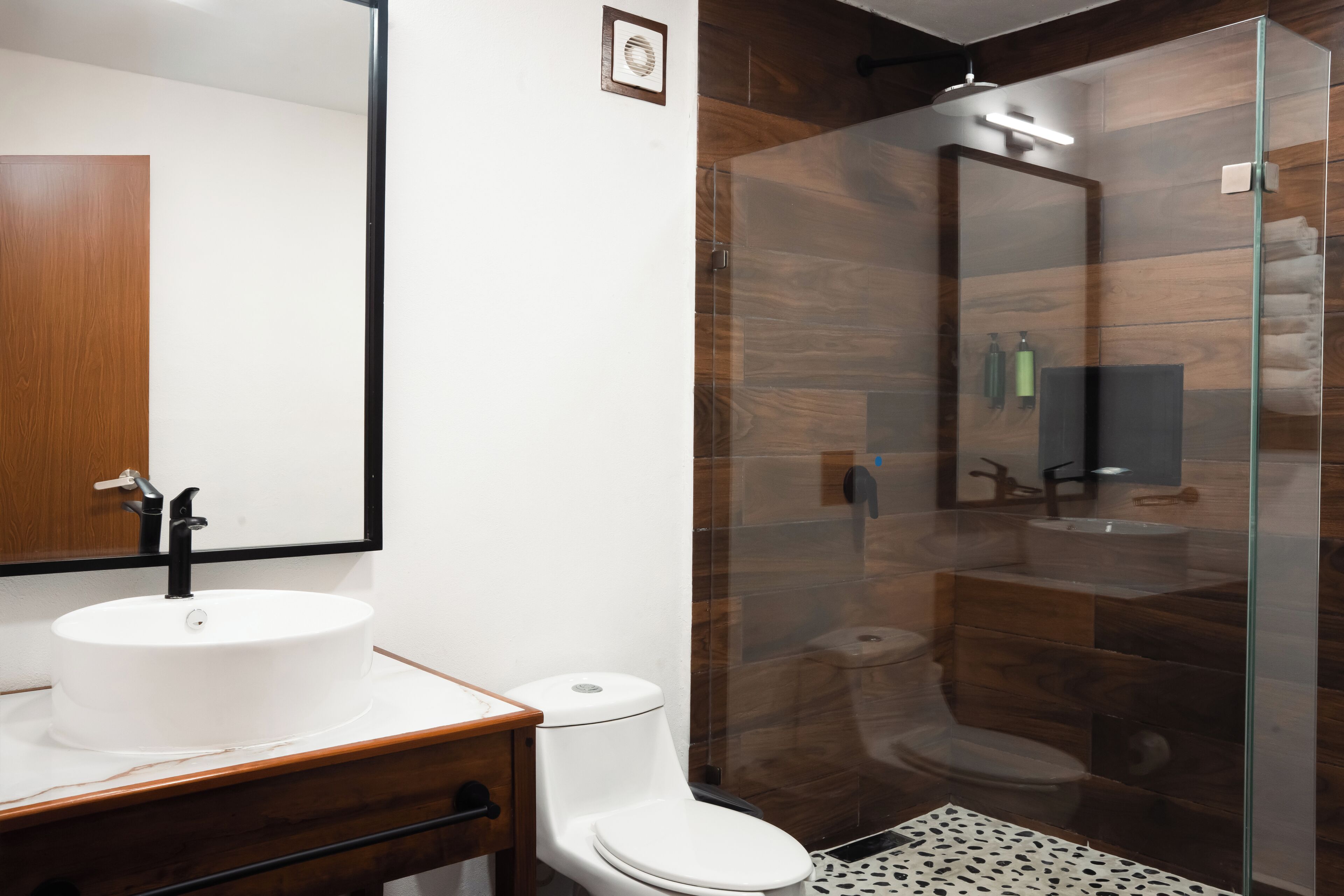 Un baño moderno con un lavamanos blanco, un inodoro y zona de ducha con mampara de vidrio.