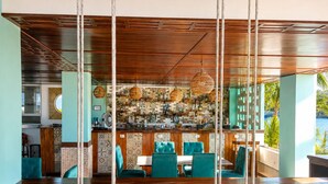 Una zona de bar con mostradores de madera, asientos tapizados en color aguamarina y paredes de baldosas con diseños.