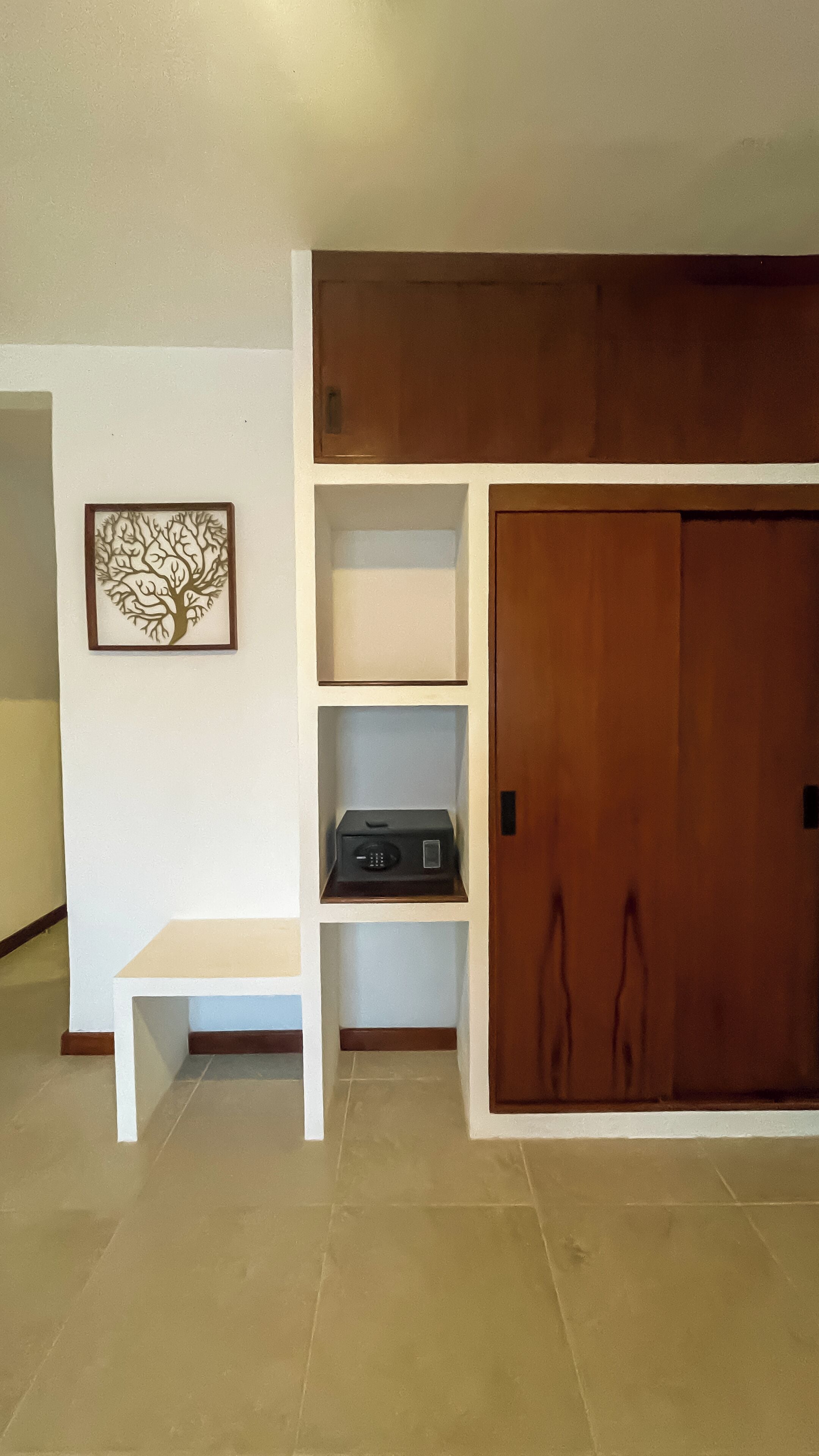 Een kamer met een houten garderobe, een witte bank en een wandplank met een decoratieve boomuitsparing.