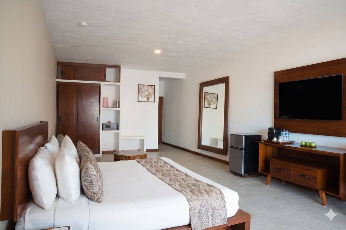 A hotel room with a bed, a TV, a minibar, a wardrobe, and a mirror.