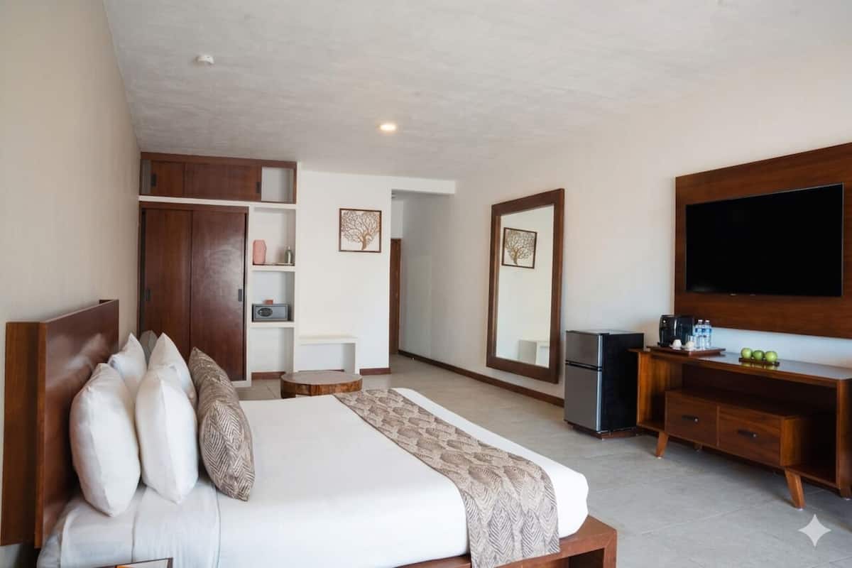 A hotel room with a bed, a TV, a minibar, a wardrobe, and a mirror.