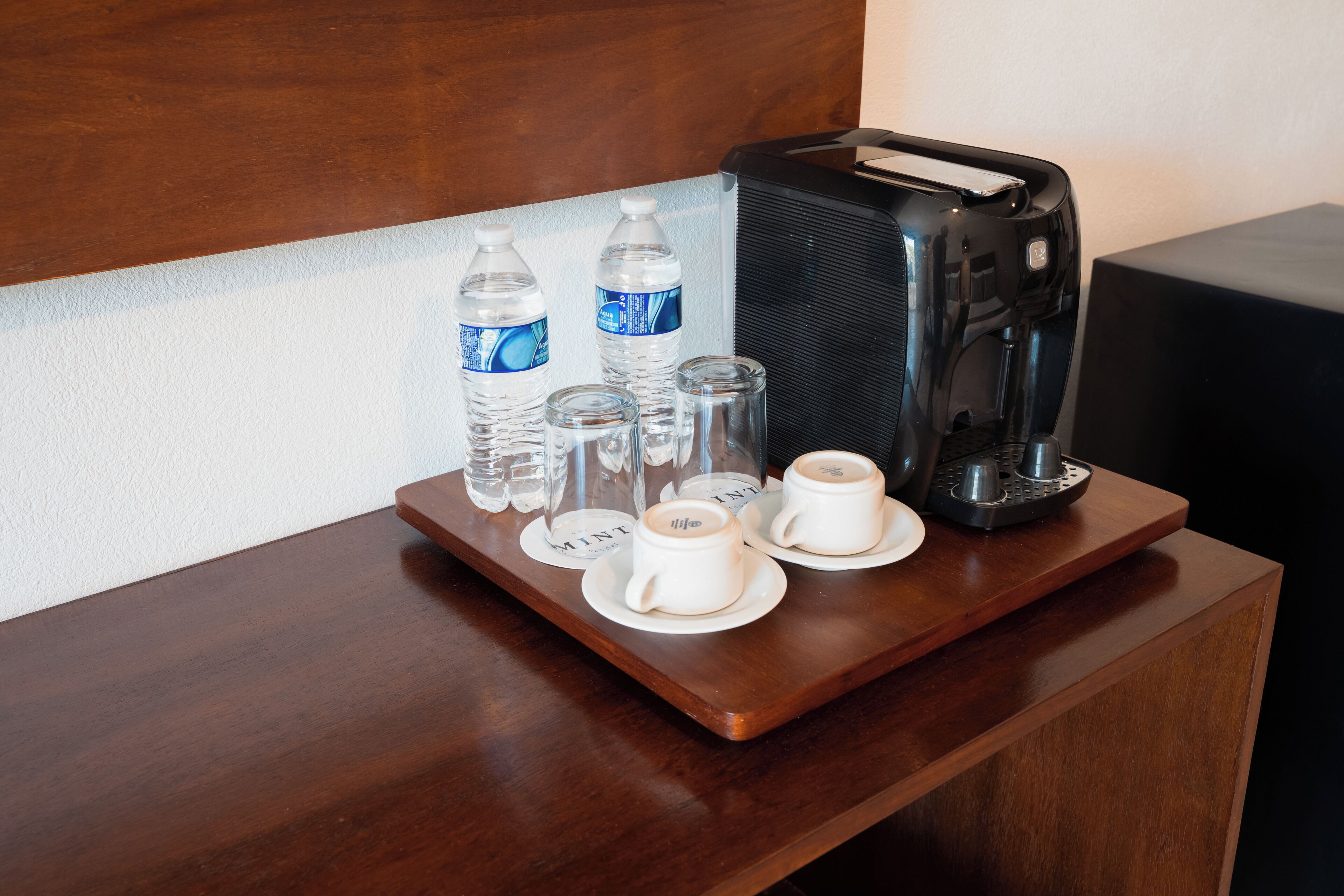 Un plateau en bois contenant des bouteilles d’eau, des verres et des tasses à café, posé sur un bureau d’hôtel.