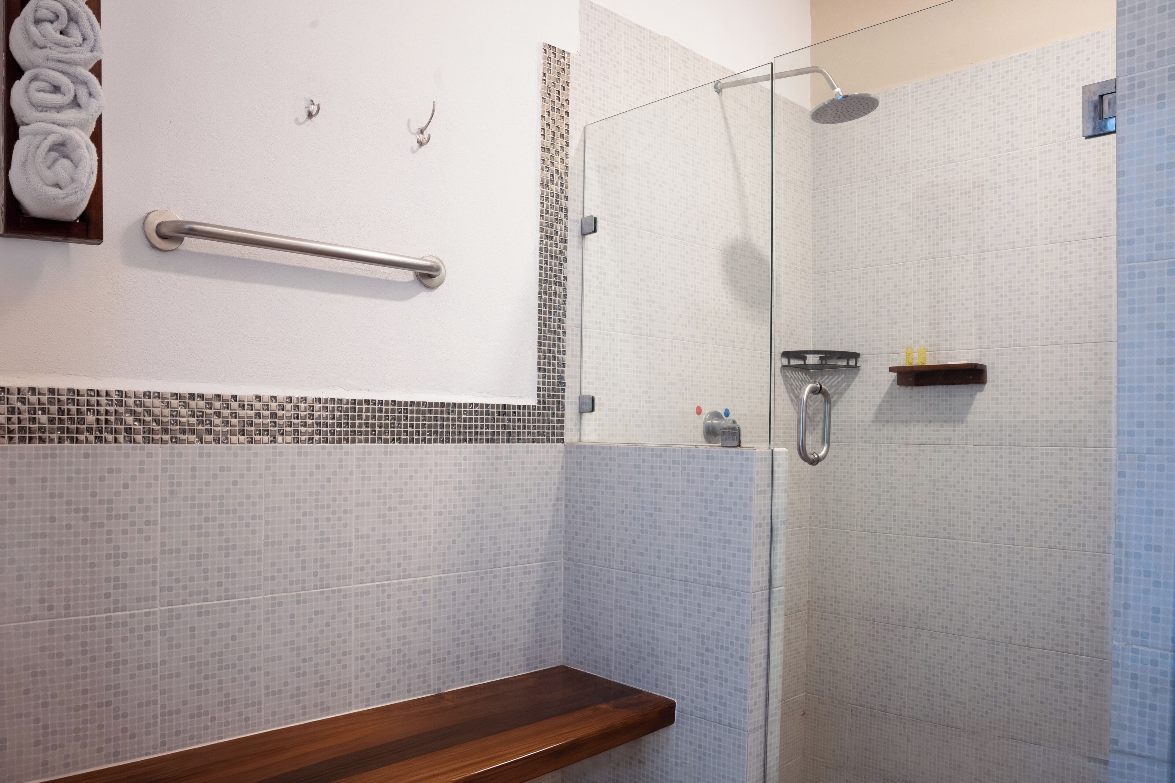 A shower with a glass door, a towel rack with towels, and a small shelf with toiletries.