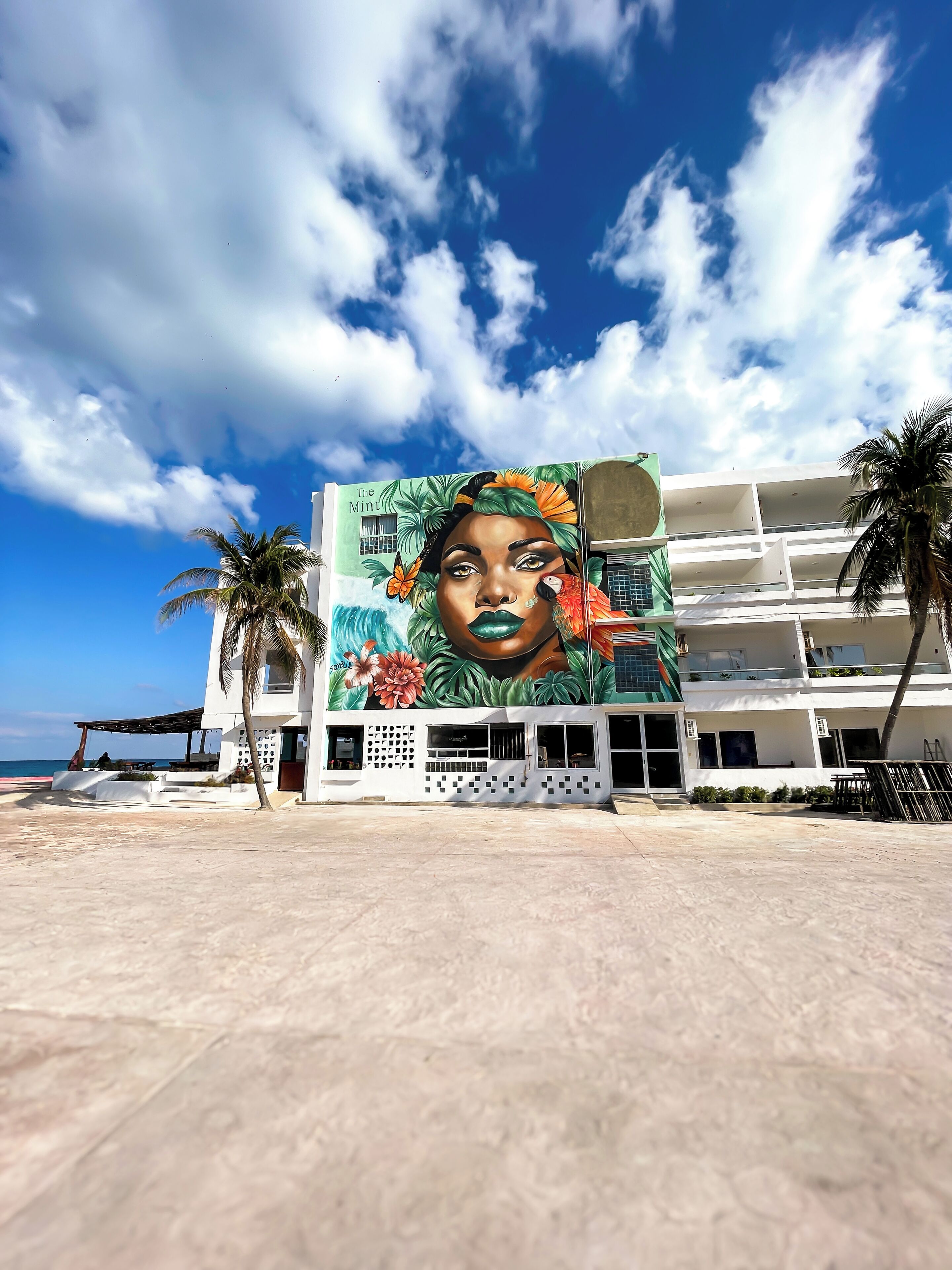A hotel with a large mural on the side, palm trees, and a view of the ocean.