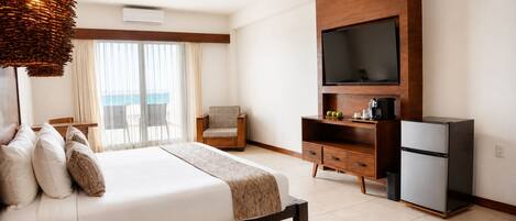 Una habitación de hotel con cama, sillón, televisión, cafetera y refrigerador.