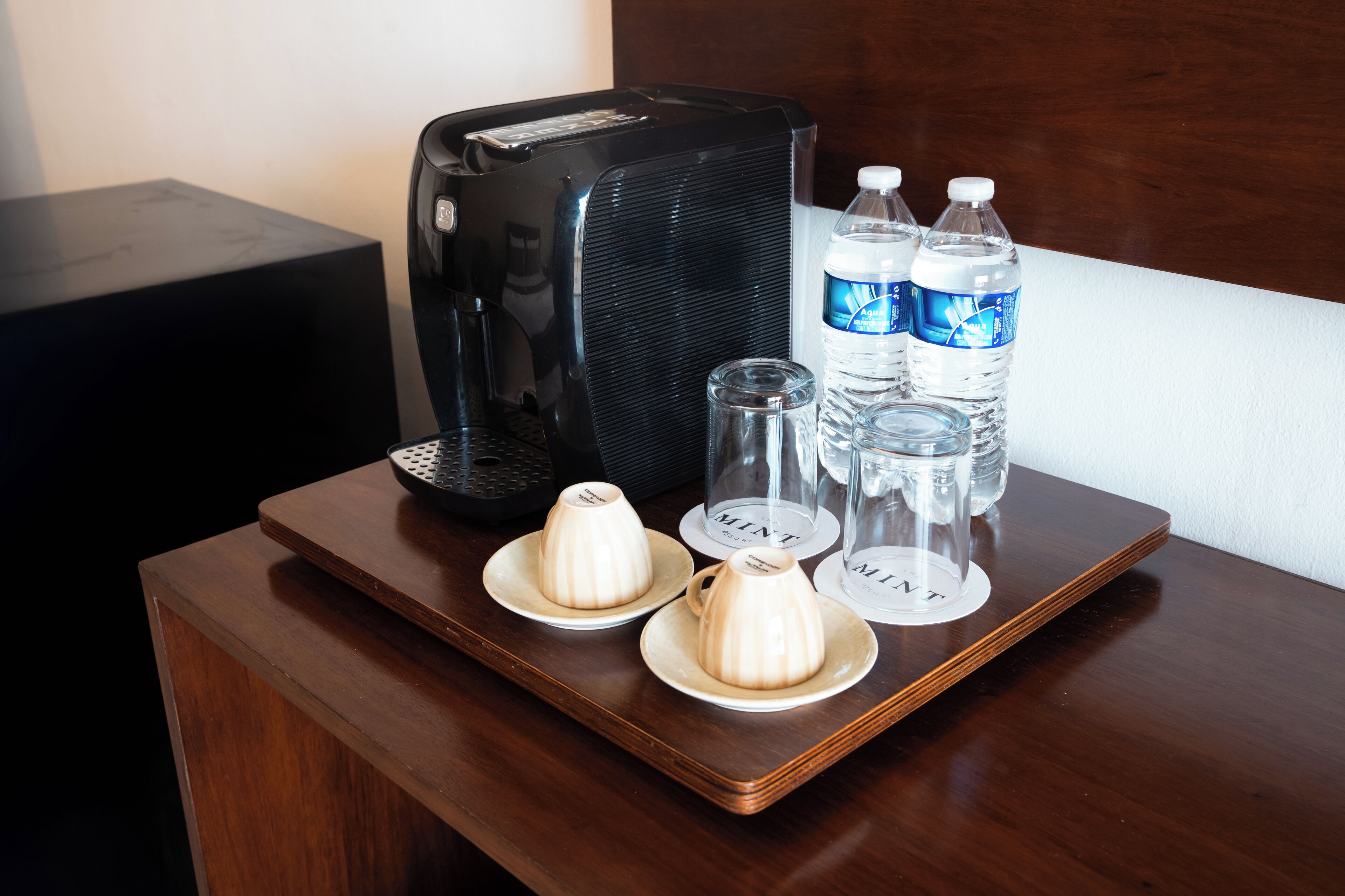 Una mesa de madera con una cafetera, dos botellas de agua y dos azucareros con tapas.