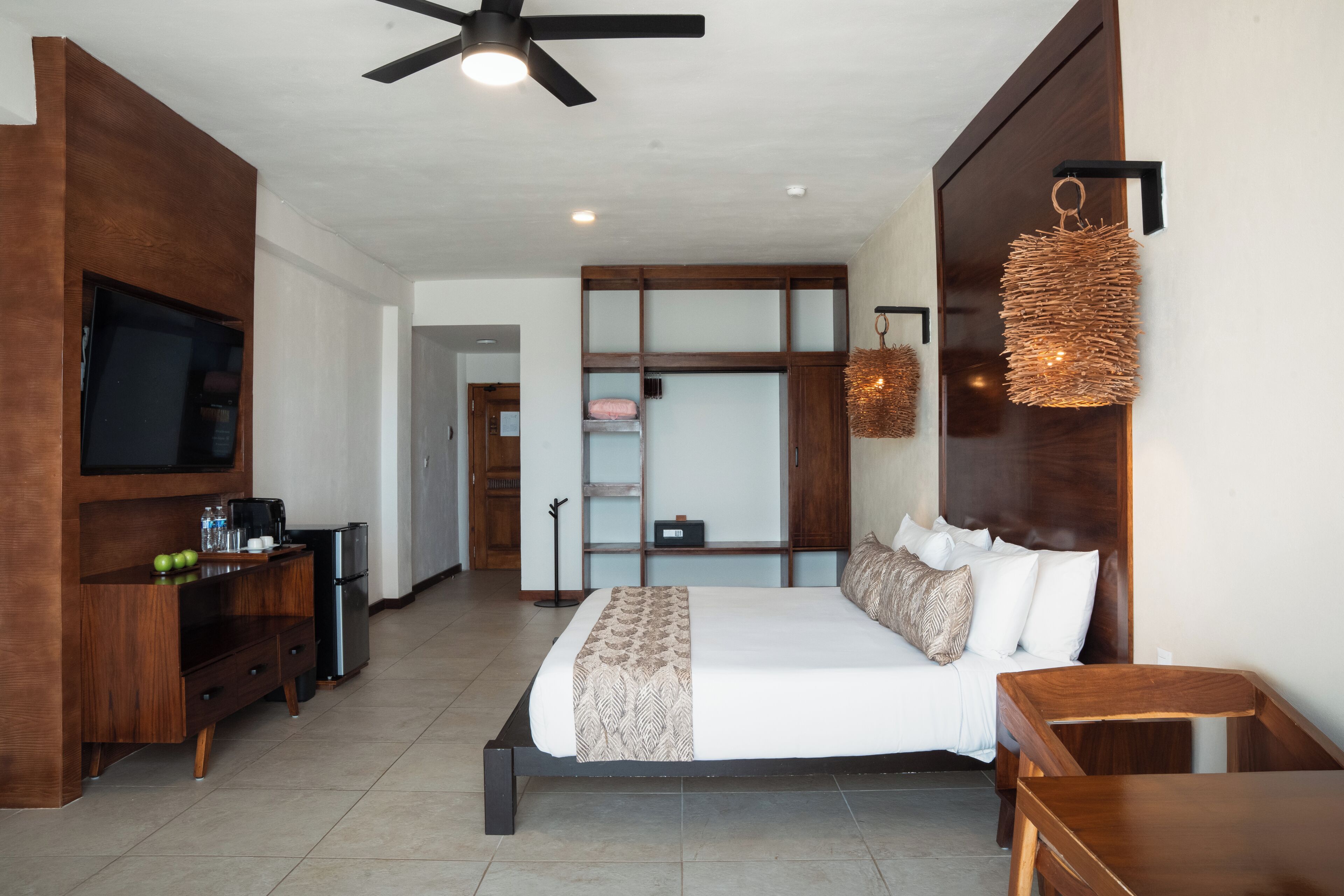 A bedroom with a bed, a TV, a desk, and a ceiling fan.