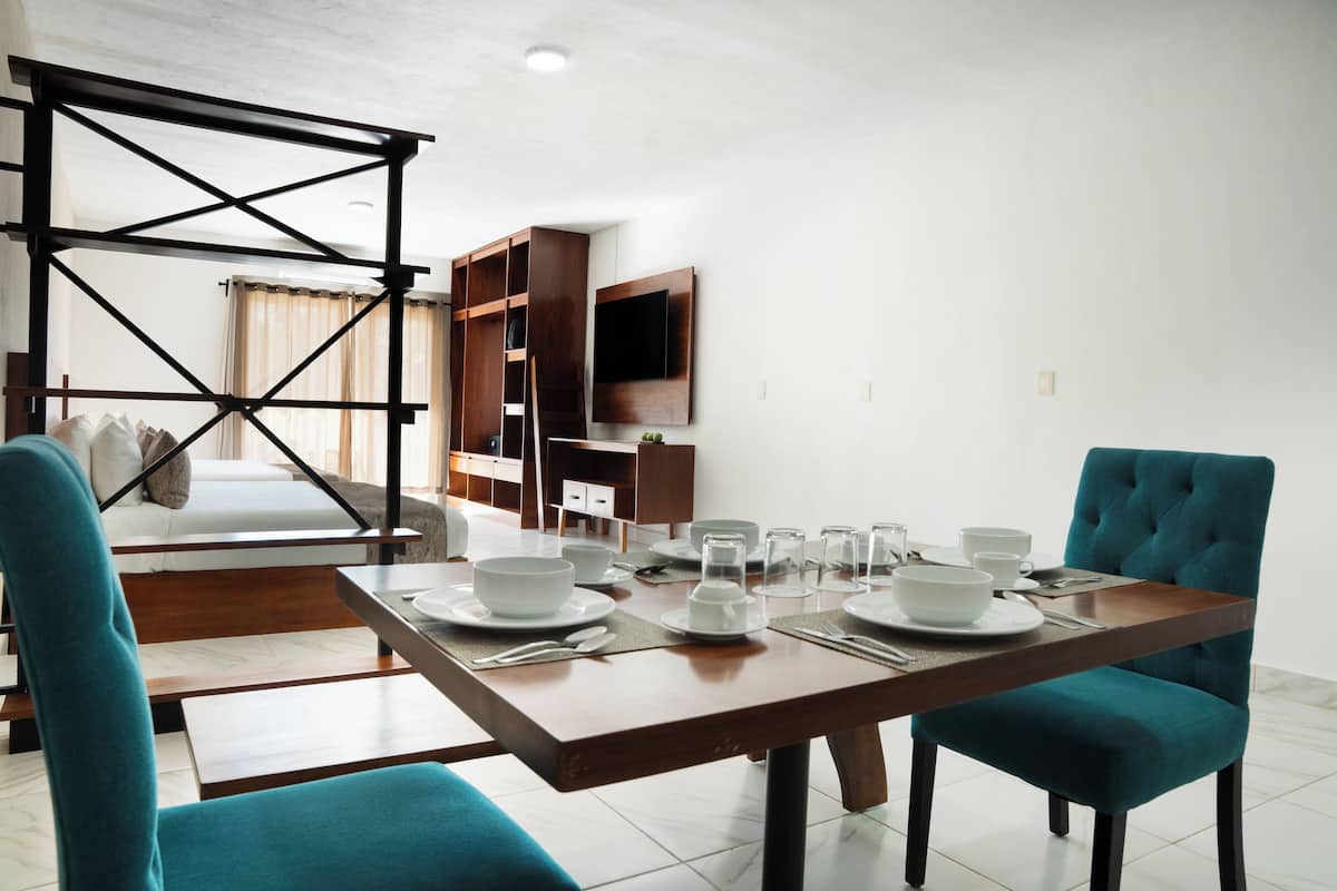 A dining area with a table set for four, a sofa, a TV mounted on the wall, and a wooden structure in the background.