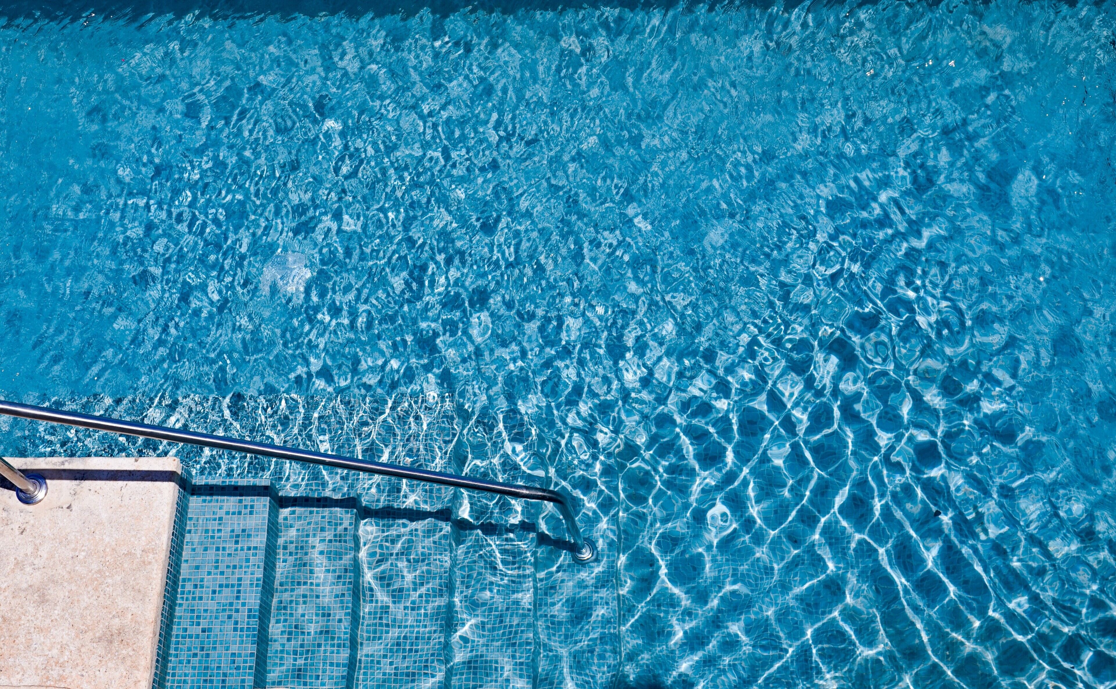 A clear blue pool with a metal ladder and tiled steps.