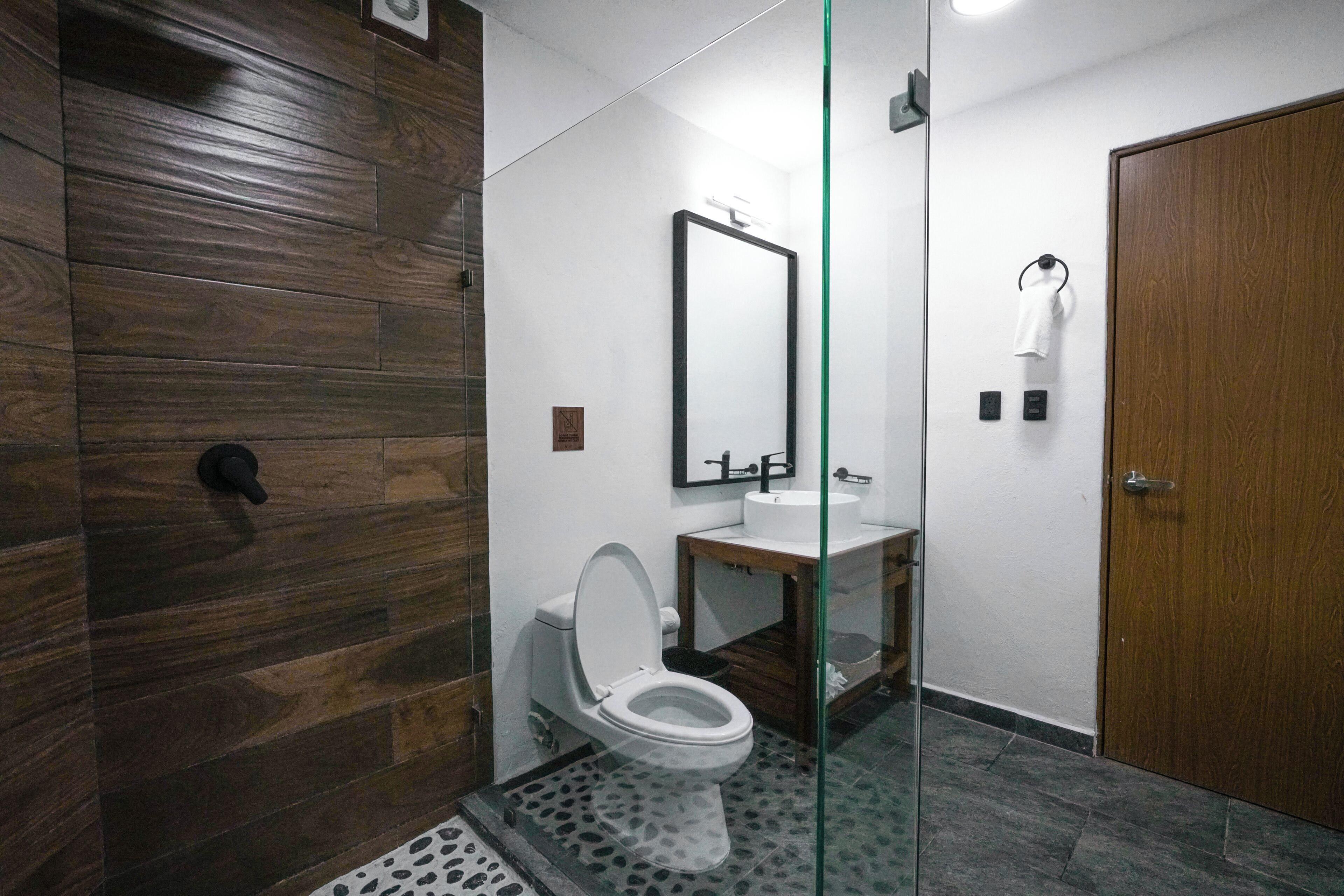 Ein modernes Badezimmer mit Holzboden, einer Glasdusche, einer weißen Toilette und einem Holzwaschtisch mit Spiegel.