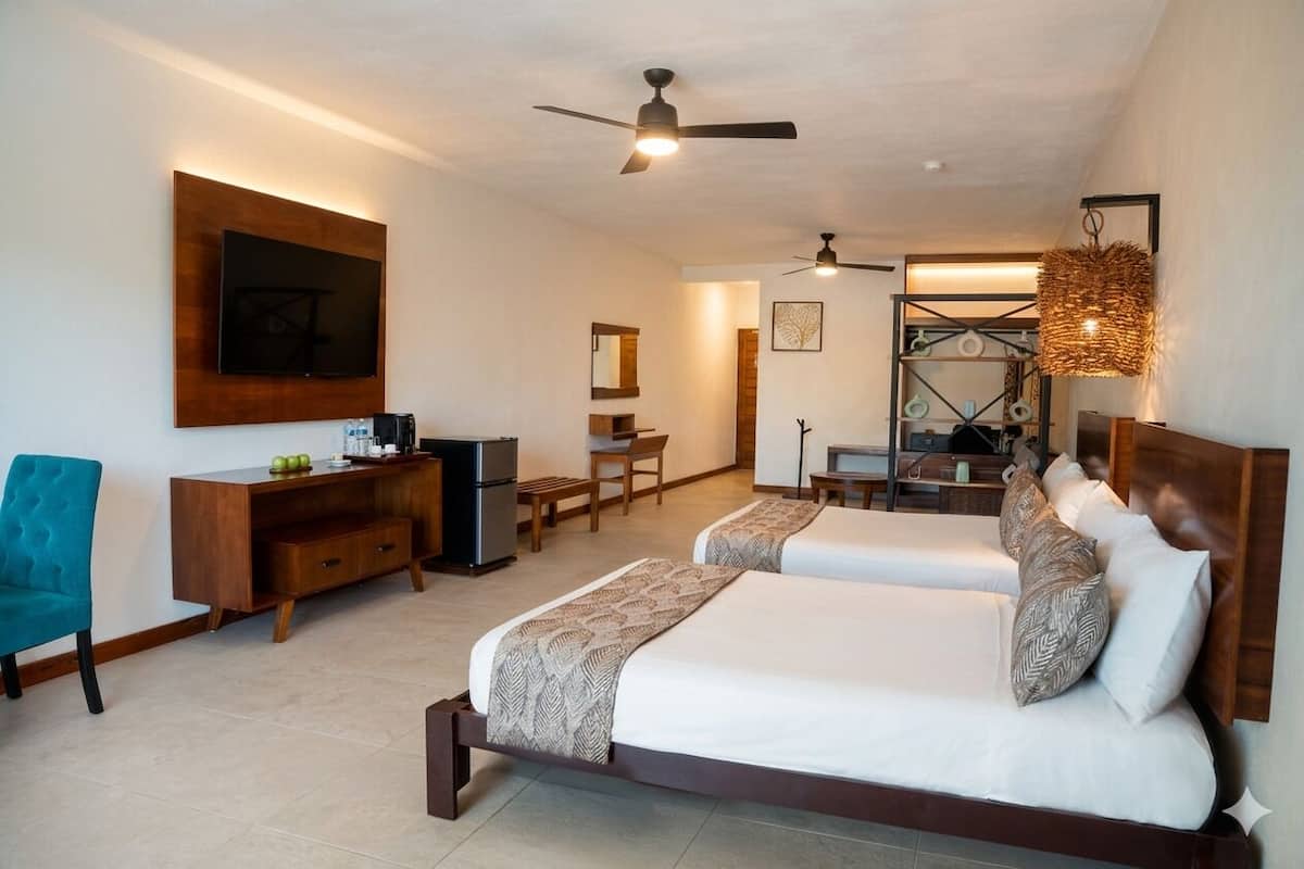 A hotel room with two beds, a desk, a chair, a television, and a ceiling fan.