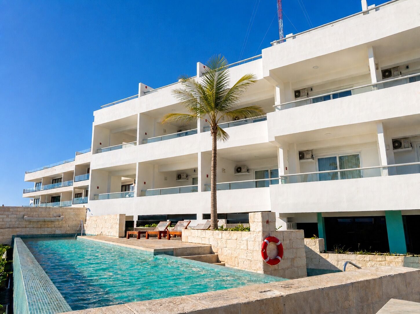Un hotel de varios pisos con piscina, balcones y una palmera.