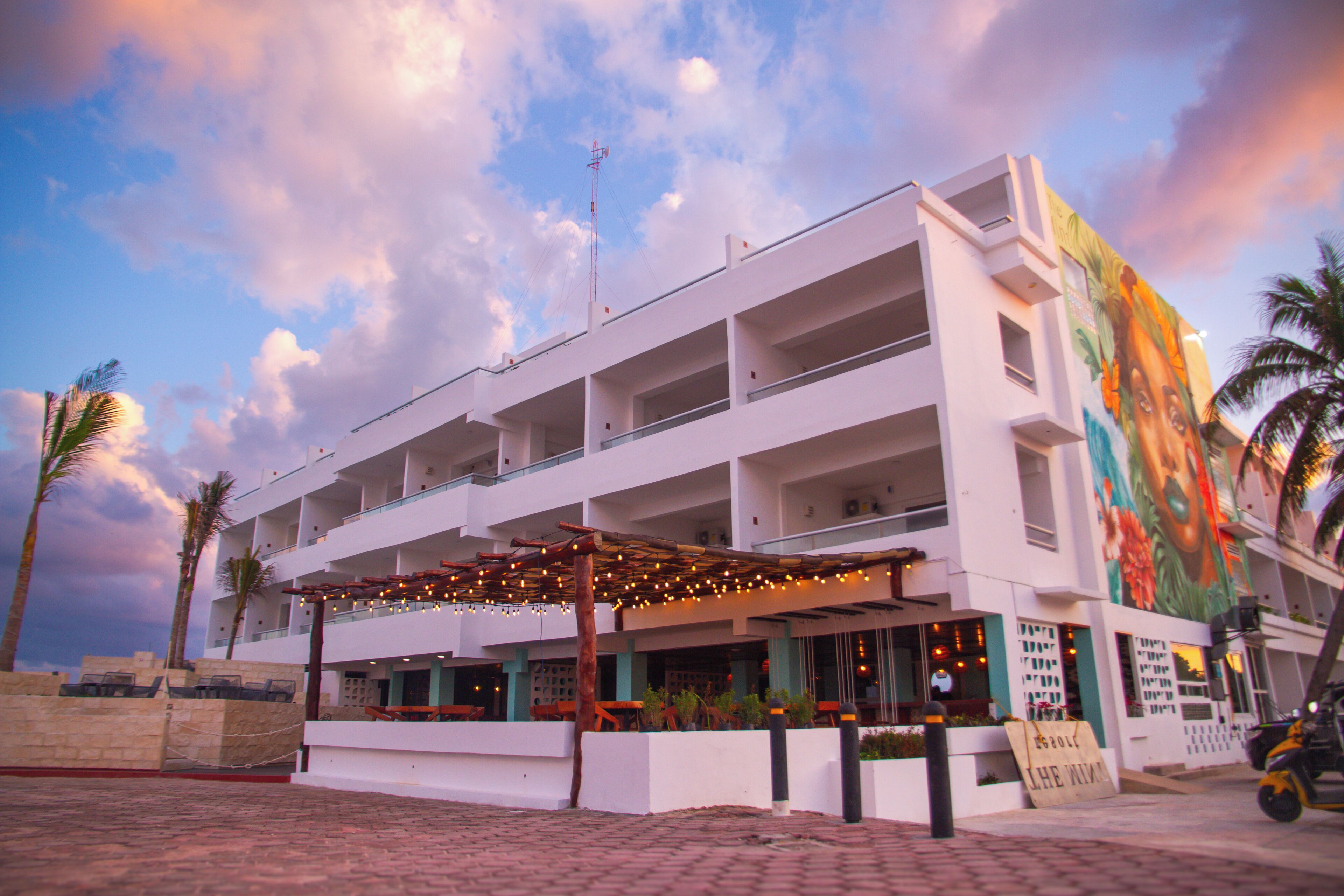 A multi-story hotel with outdoor seating, a mural, and a clear view of the sky.