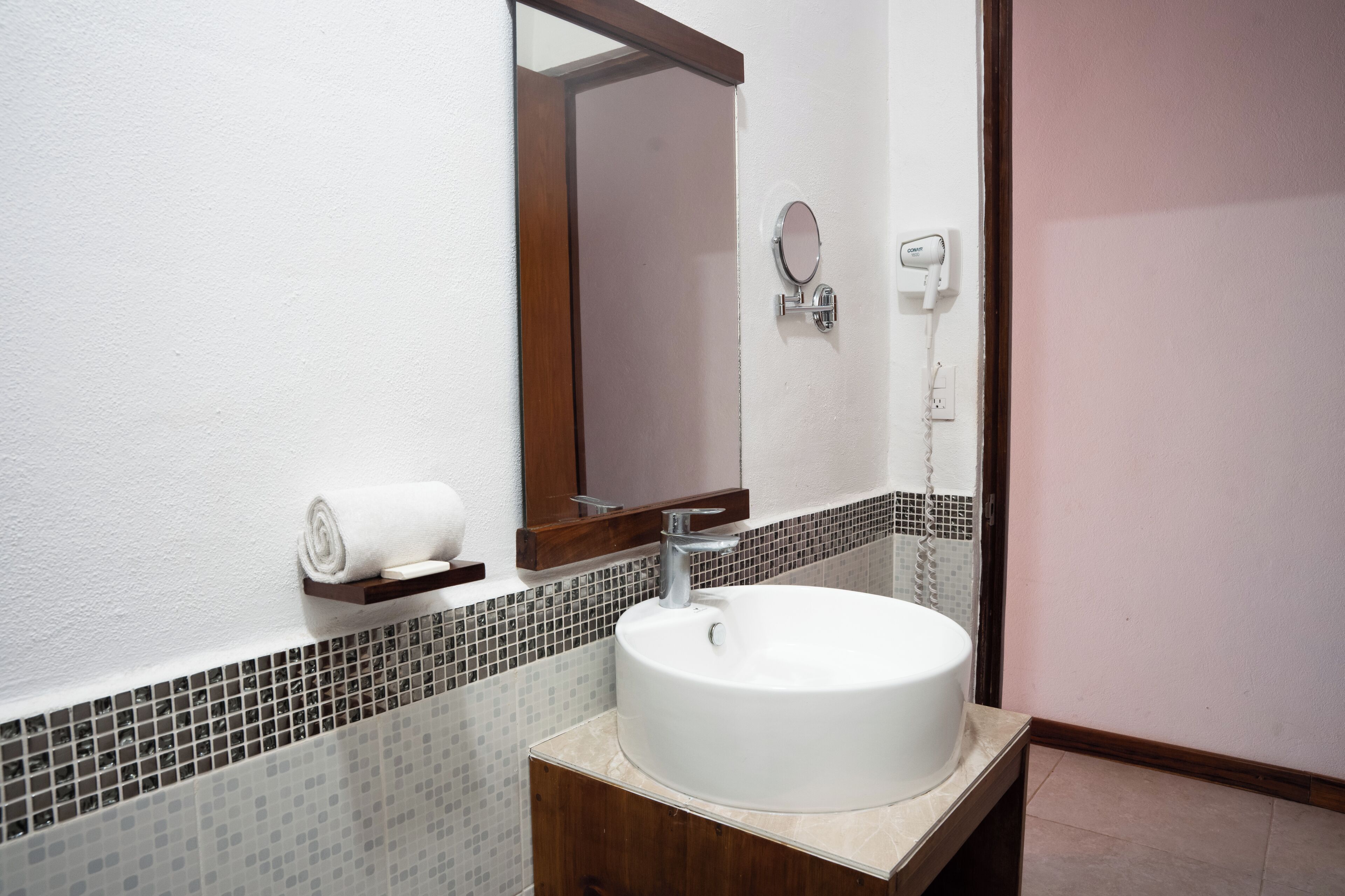 A bathroom with a white sink, a mirror, a towel, and a hairdryer on the wall.