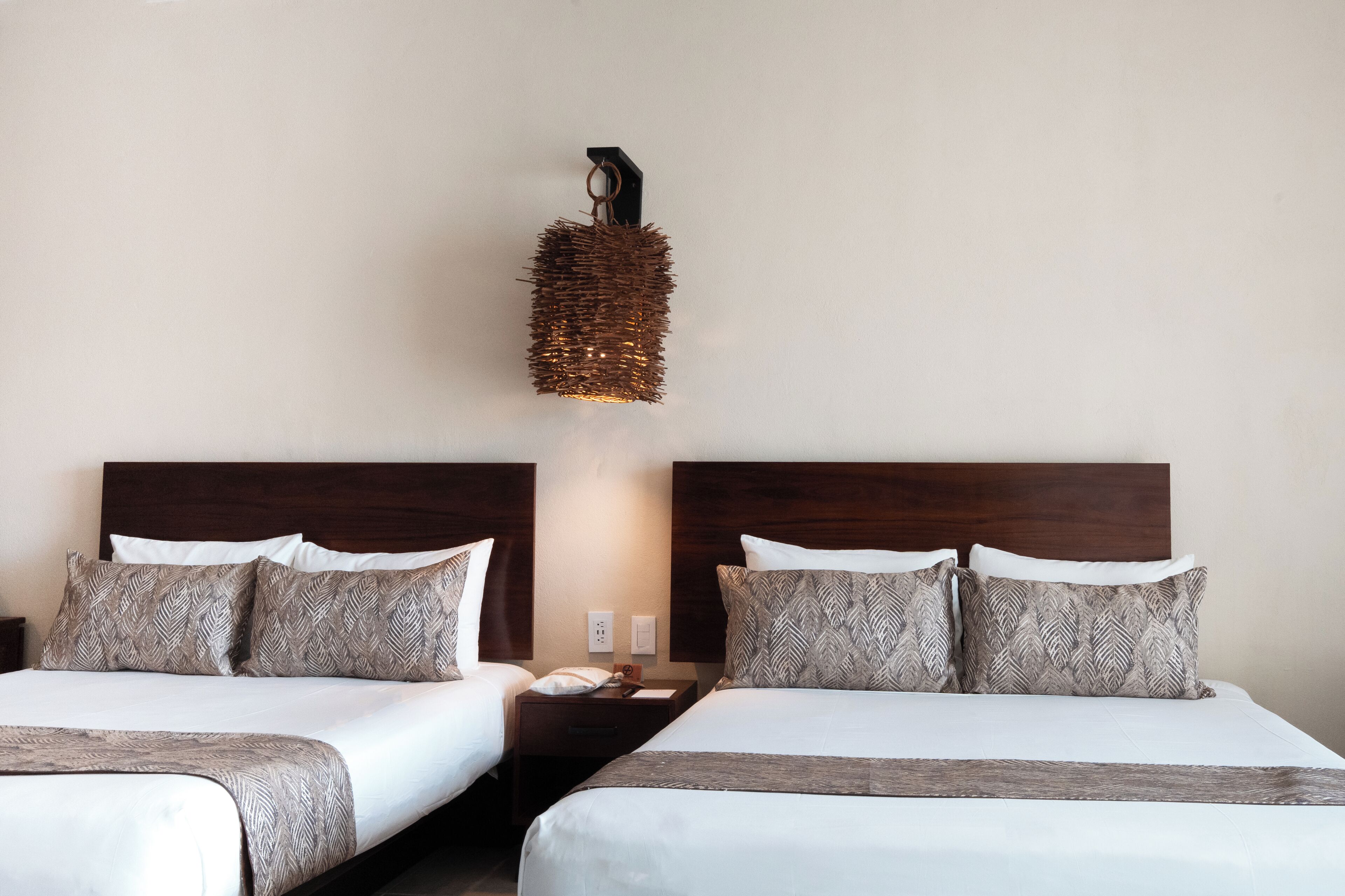 Een hotelkamer met twee bedden, een nachtkastje, een wandlamp en een houten hoofdeinde.