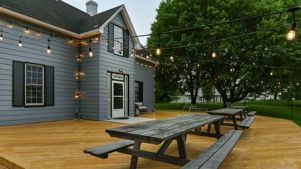 A gray house with a wooden deck and picnic tables.