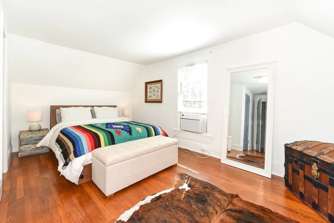 A bedroom with a bed, bedside table, lamp, and a large mirror.