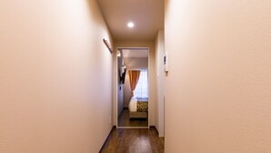 Ein schmaler Korridor mit Holzdielen führt zu einem Schlafzimmer mit Bett und einem fensterbepflanzten Fenster.