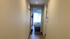 Ein schmaler Korridor mit Holzboden, der zu einem Zimmer mit Bett und Fenster führt.