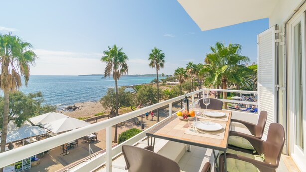 Un balcón con una mesa lista para dos personas, con vista a la playa y al mar.