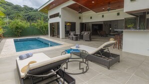 Une maison moderne dotée d’une piscine, d’un espace salon extérieur et d’un bar.