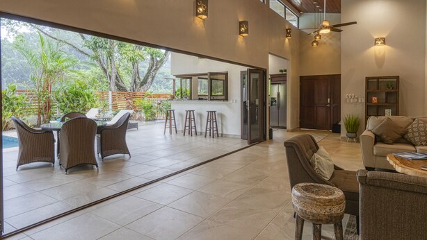 Un vaste espace de vie avec une grande porte vitrée donnant sur un patio extérieur, aménagé avec des fauteuils en osier et un coin bar.