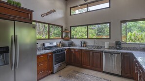 Une cuisine moderne avec des meubles en bois, des appareils électroménagers en acier inoxydable et de grandes fenêtres offrant une vue sur la verdure.