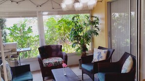 Una habitación luminosa con una ventana grande, muebles de mimbre, una planta en maceta y un ventilador de techo.