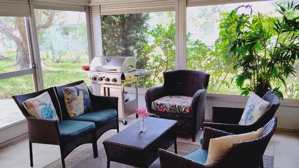 Un patio cubierto con mobiliario de mimbre, una parrilla y vistas a la vegetación.