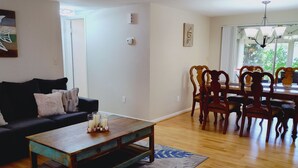 Una sala de estar con una mesa de centro de madera, un sofá negro, una zona de comedor con sillas de madera y un ventanal grande.