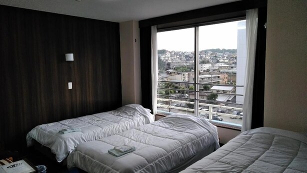 A hotel room with two beds, a large window with a city view, and a dark wooden headboard. - Hotel Takanoya (Hadano)