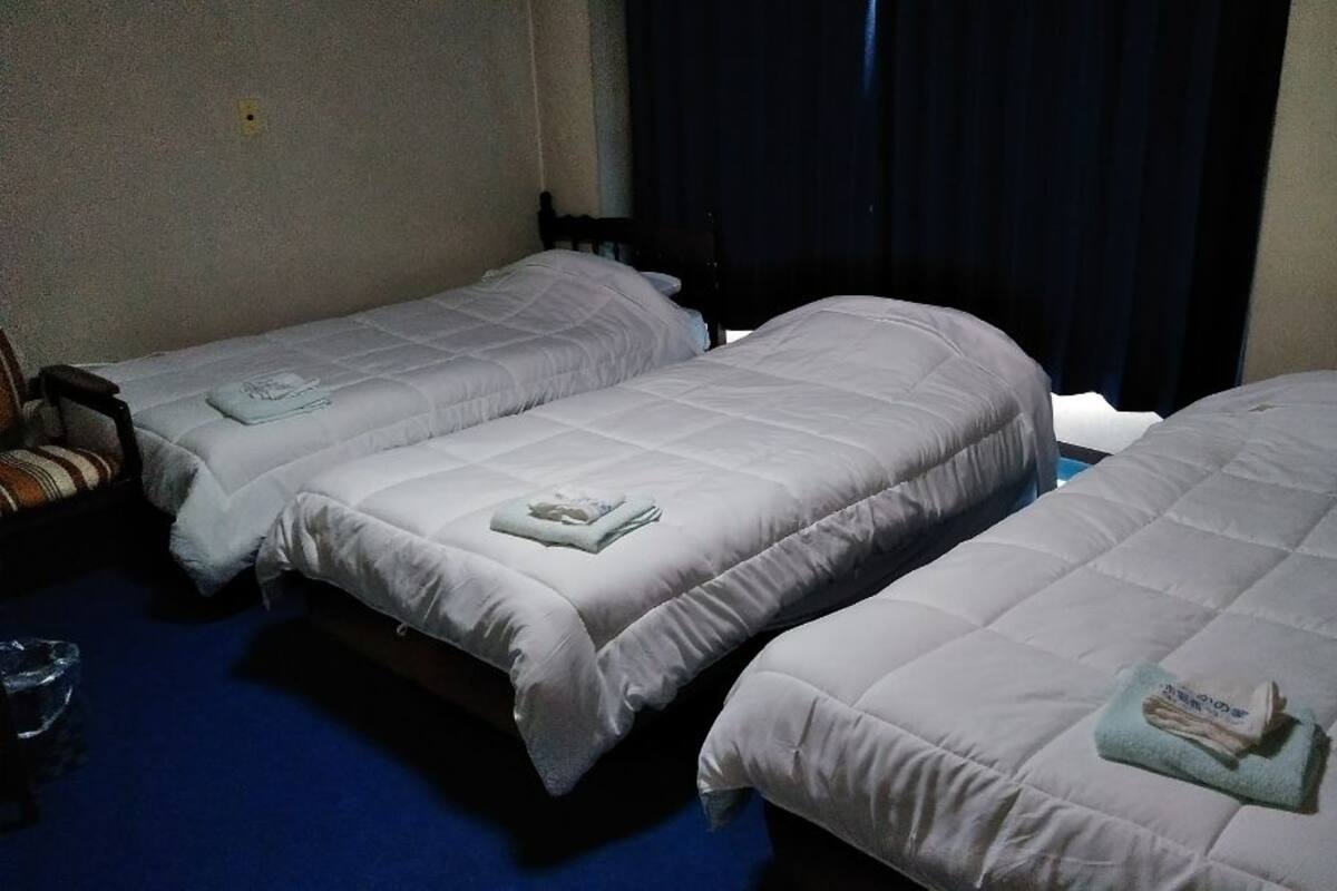 A hotel room with two single beds, a small table, and a chair.