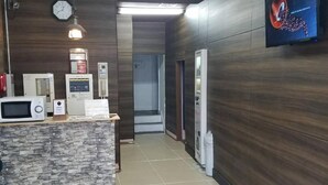 A reception area with a stone counter, a clock, and a television mounted on the wall. - Hotel Takanoya (Hadano)