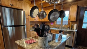 Una cocina moderna con armarios de madera, electrodomésticos de acero inoxidable y utensilios colgando.