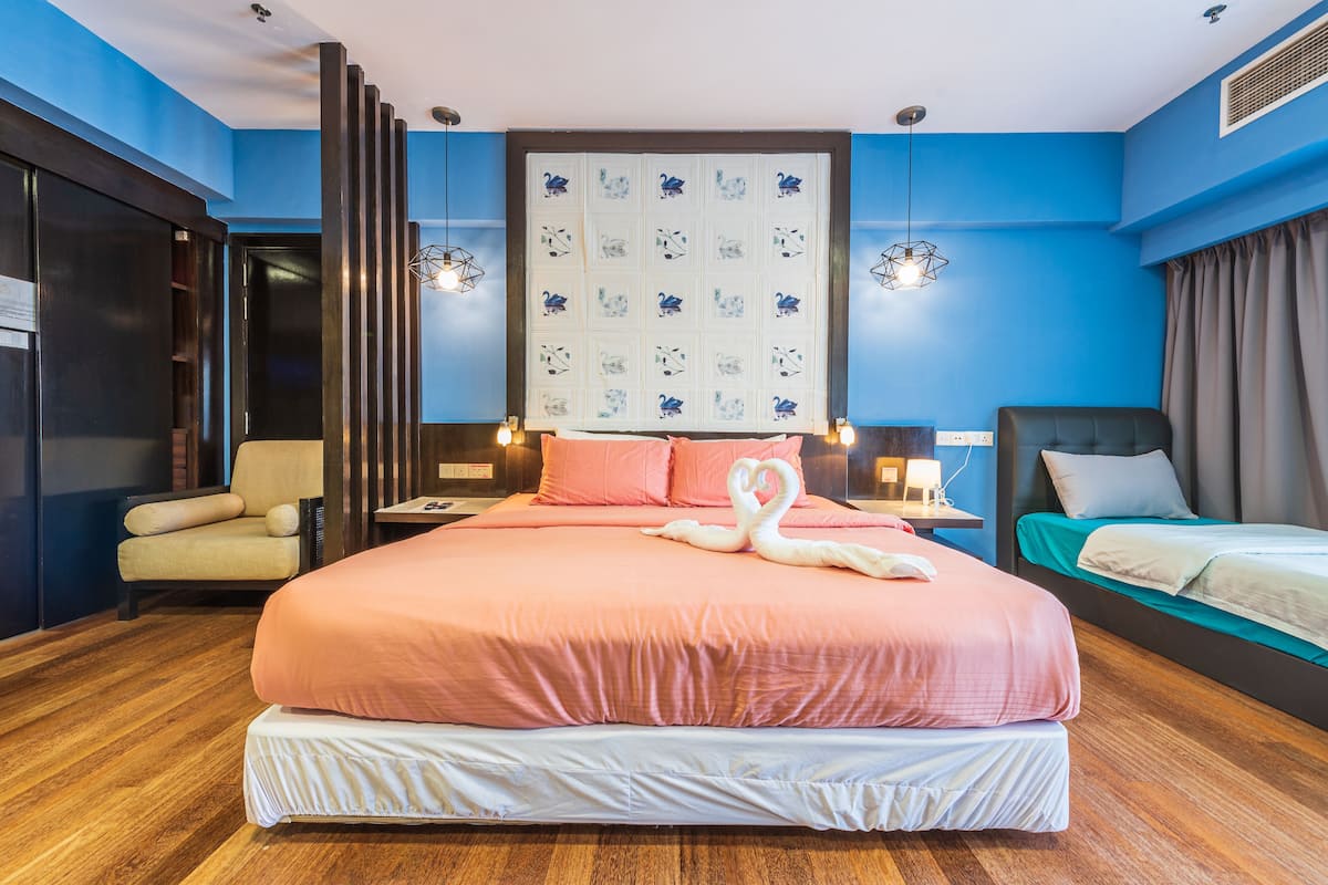 A large bed with pink bedding, a wooden floor, a wall with a blue and white pattern, and a chair.