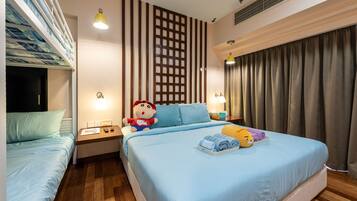 A hotel room with a bunk bed, a large bed with a blue bedspread, a wooden floor, a decorative wall panel, and a window with curtains.